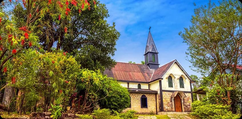 Charming stone church surrounded by lush greenery and red flowers in Mawlynnong