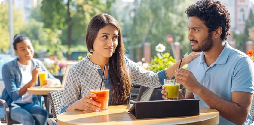 Brother and sister sitting at an outdoor cafe with juice and a tablet